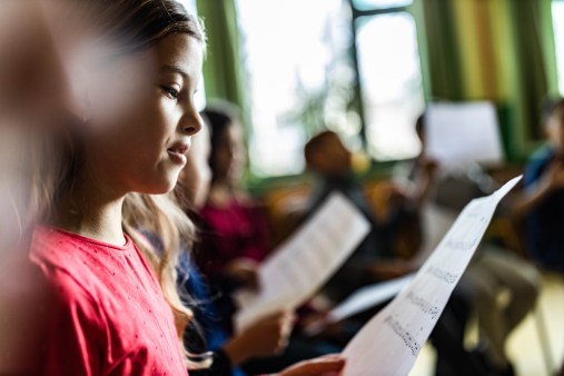 Girl holds sheet music with kids singing.